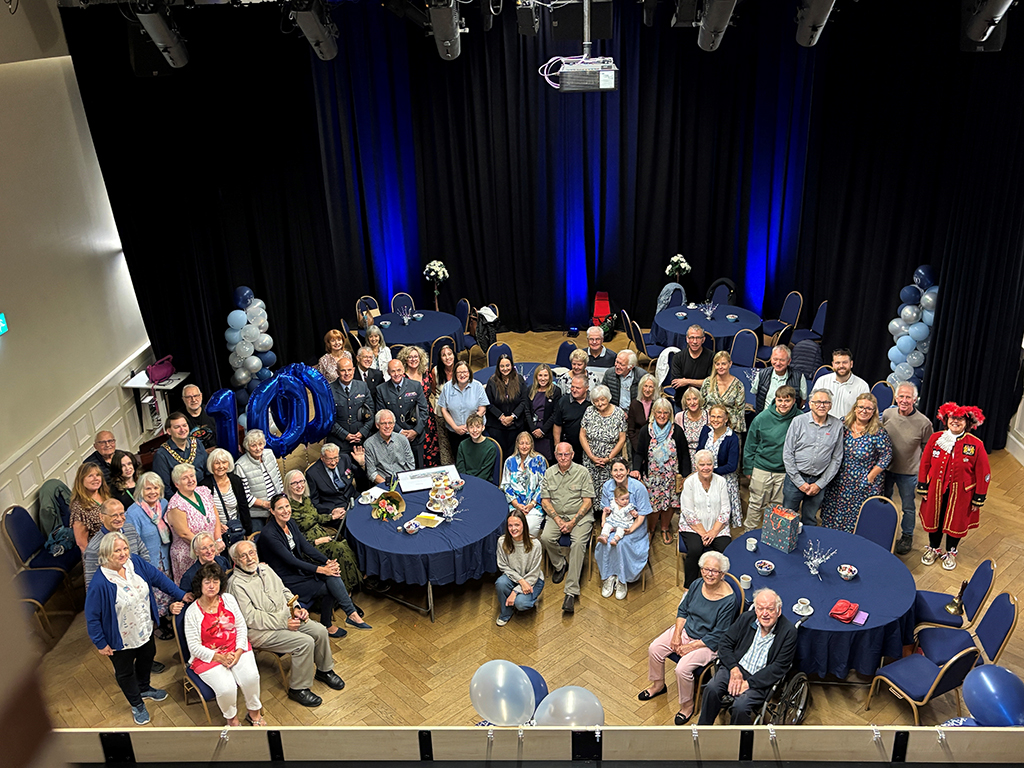 A view from the Witney Corn Exchange hall balcony, looking down over the seated Denis Bishop, surrounded by family, friends and RAF personnel.